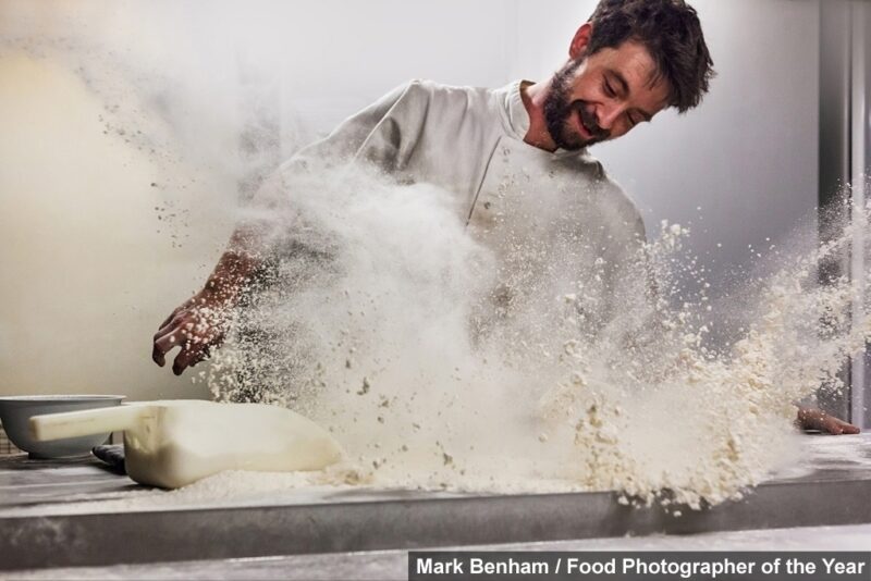 Foto de cozinheiro de branco levantando nuvem de farinha
